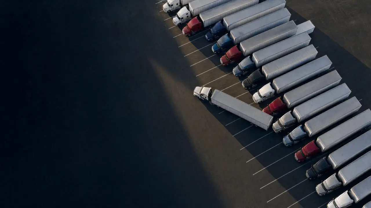 Aerial view of a truck lot with tractor-trailers in many colors, one pulling out of its row.