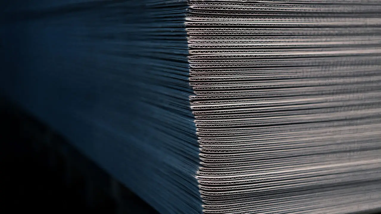 The fluted edges of stacked plain corrugated boards in cool side light.